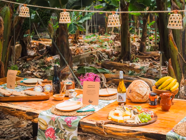 Holztisch unter den Bananenstauden, gedeckt mit palmerischem Käse, Brot, Mojo, Wein und Bananen, beleuchtet von Korblaternen